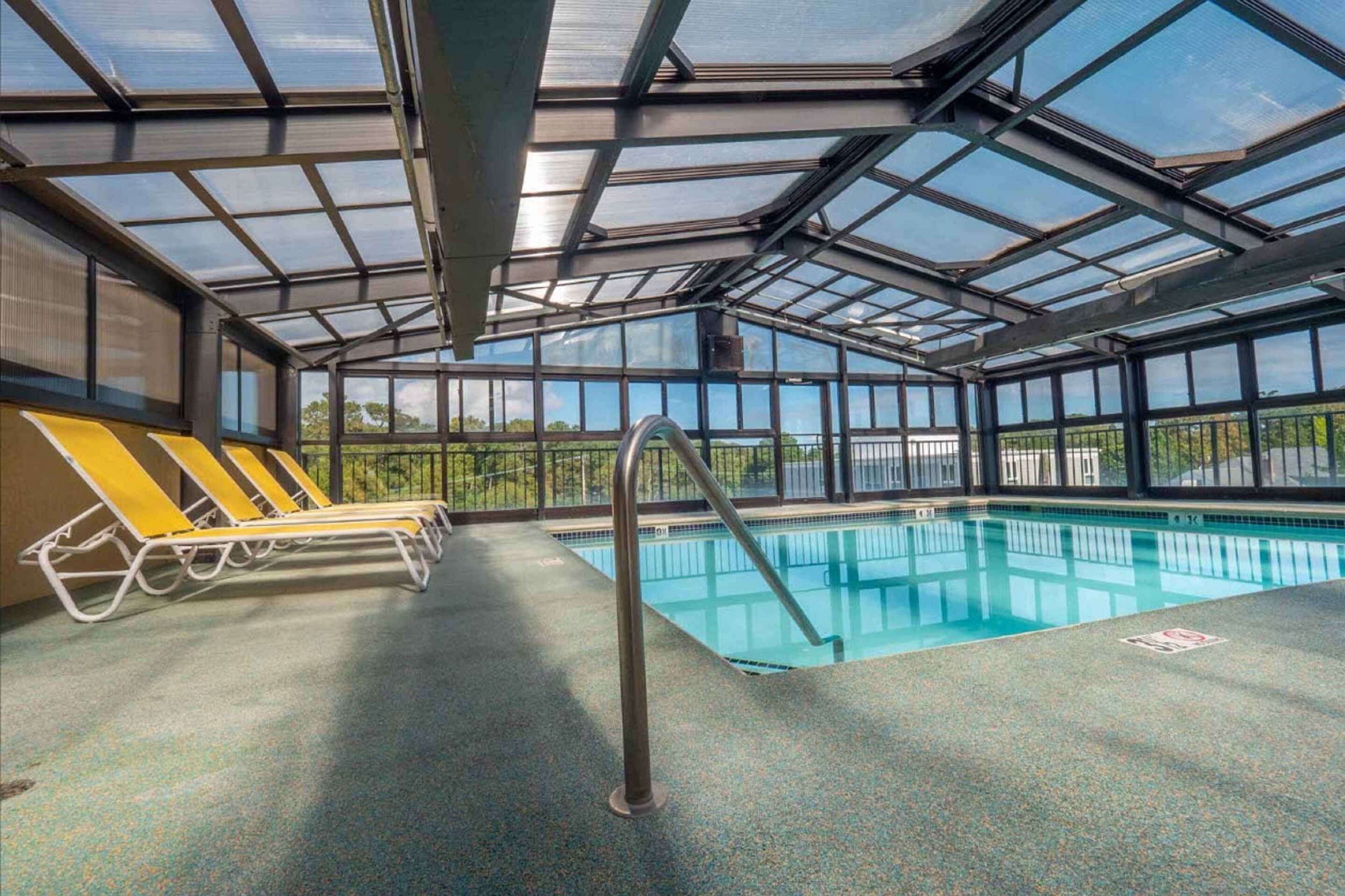 An indoor swimming pool with clear glass ceilings, yellow lounge chairs, and a metal pool ladder.