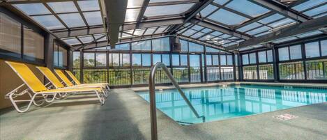 An indoor swimming pool with clear glass ceilings, yellow lounge chairs, and a metal pool ladder.