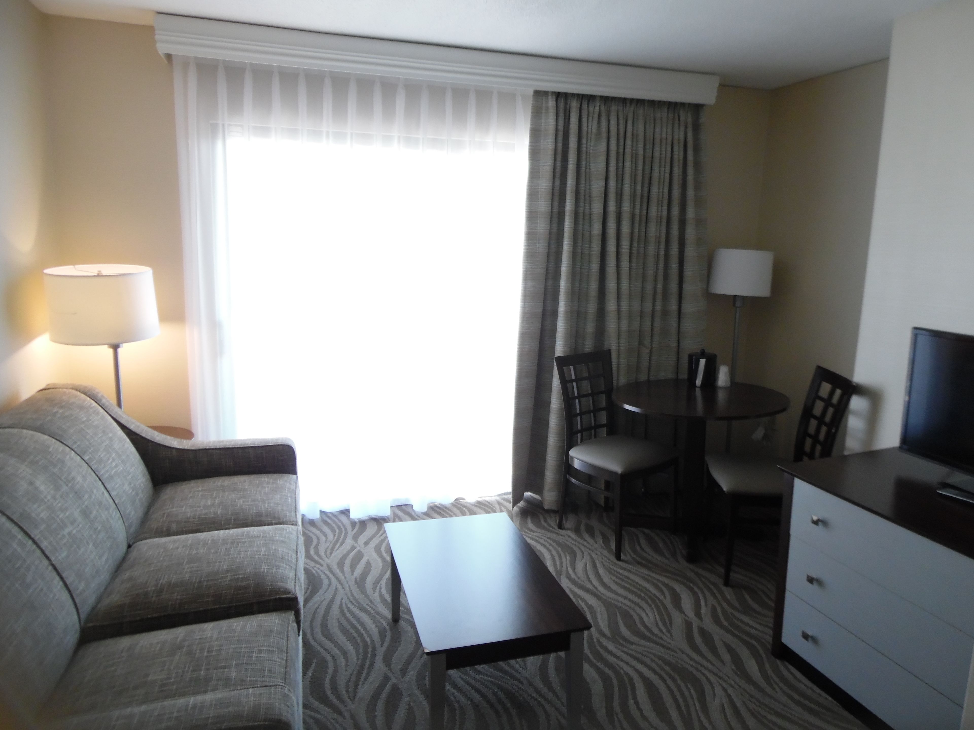 Una habitación de hotel con sofá, una pequeña mesa, televisión, escritorio y sillas.