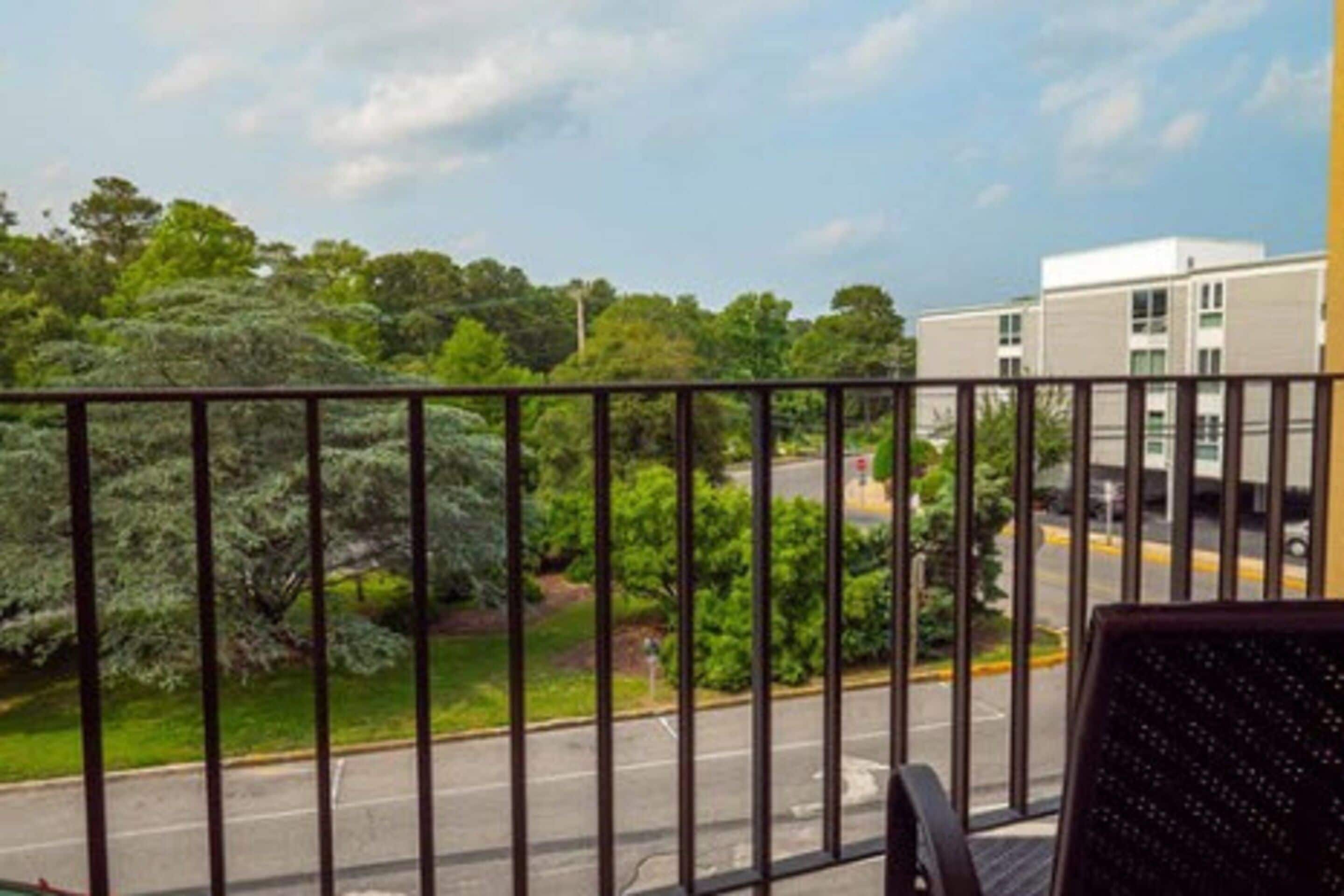A balcony with a metal railing, a chair, and a view of a road and greenery.