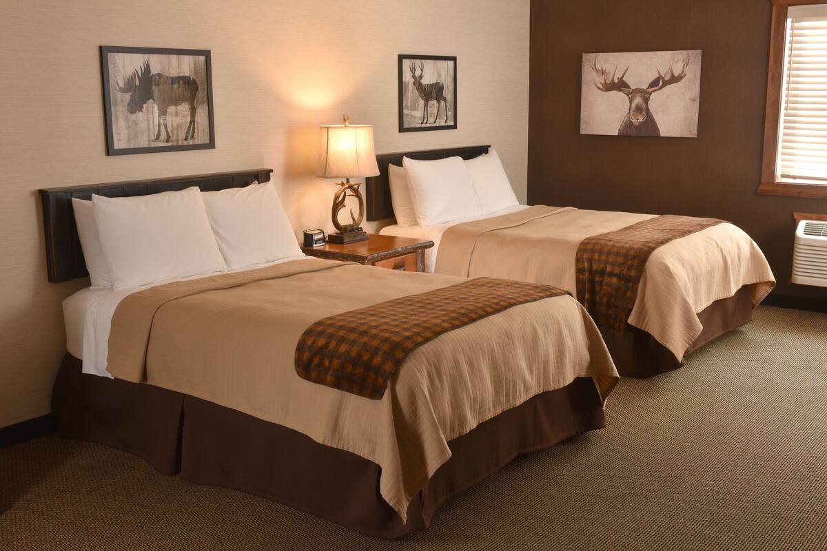 Ein Hotelzimmer mit zwei Betten, einem Nachttisch mit Lampe und Hirsch-Wandbildern.