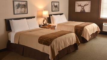 A hotel room with two beds, a nightstand with a lamp, and wall art of deer.