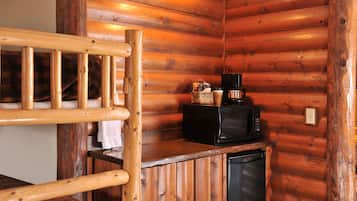 Interior de una cabaña de madera con una litera, un microondas y un refrigerador pequeño.