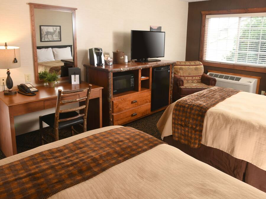 A hotel room with two beds, a desk with a computer, a television, and a window with blinds.
