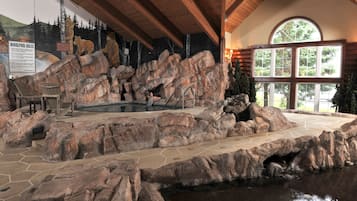 Relax in a tranquil indoor space surrounded by natural rock formations and a soothing pool, accompanied by Adirondack chairs.