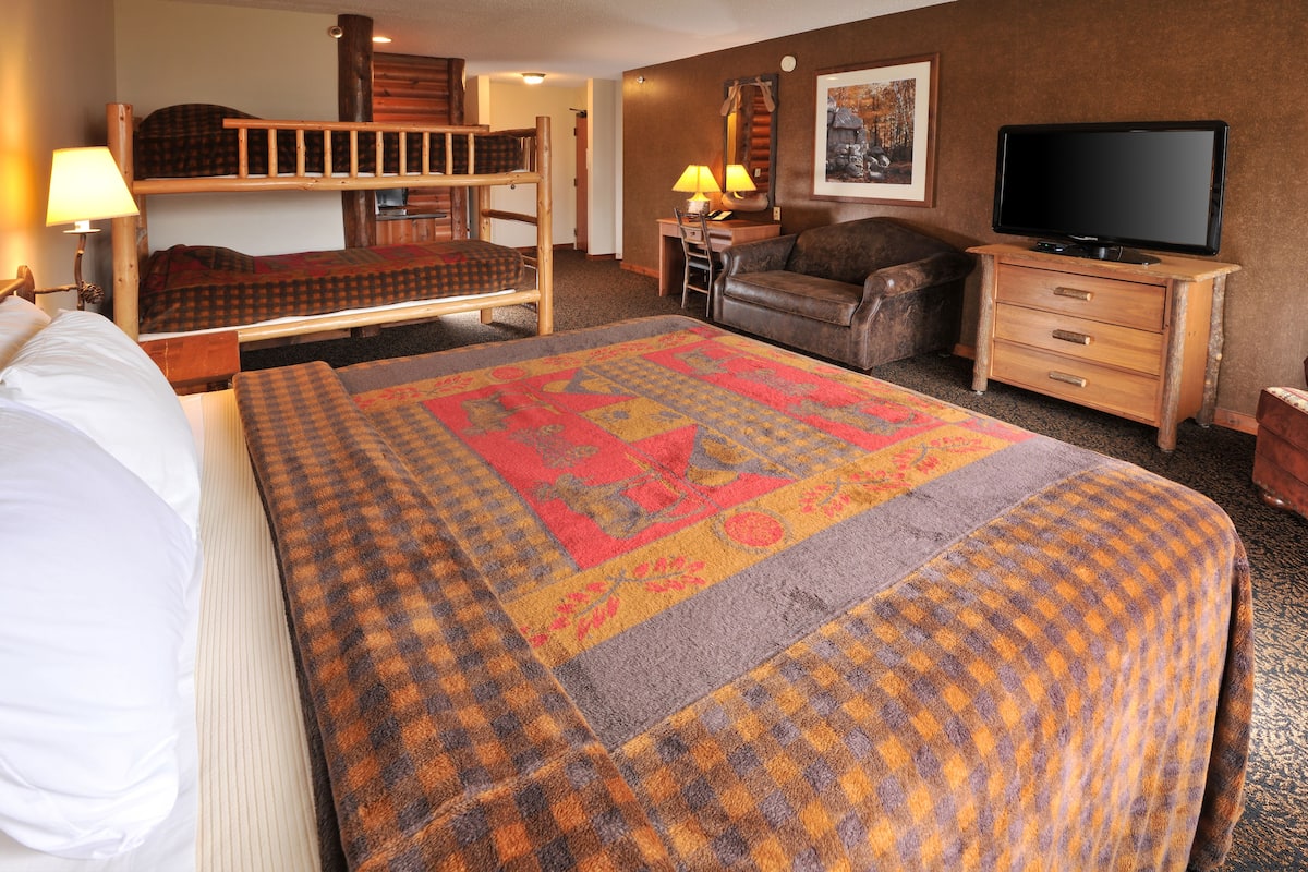 Ein Hotelzimmer mit Etagenbett, Schreibtisch mit Stuhl, Fernseher und einem großen Überwurf.