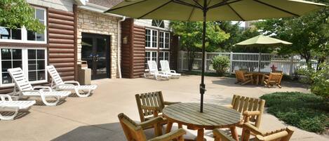 Eine Terrasse mit Holzmöbeln, darunter ein Tisch und Stühle, sowie ein großer Sonnenschirm, der Schatten spendet.