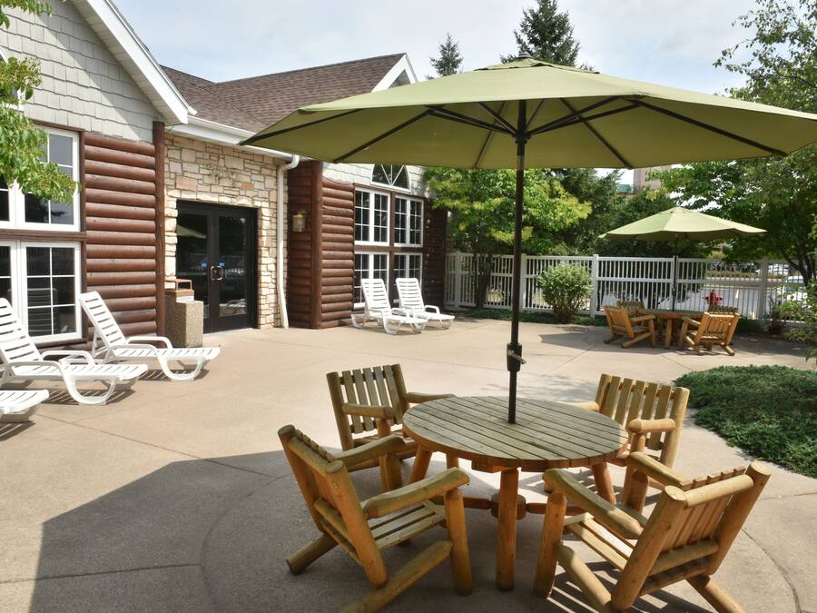 Een terras met houten meubels, waaronder een tafel en stoelen, en een grote parasol voor de schaduw.