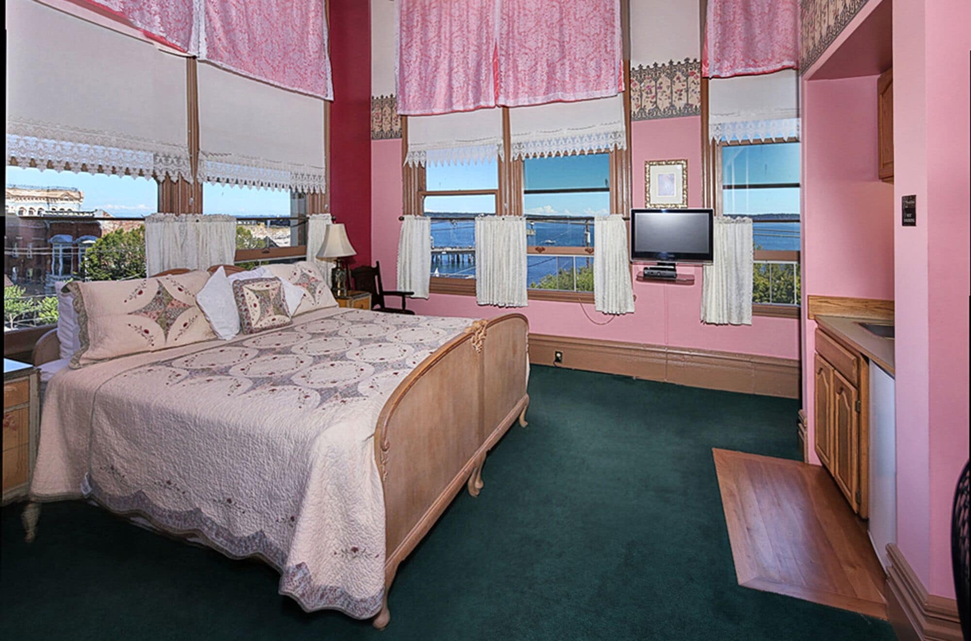 A bedroom with a large bed, a television, and a view of the sea through the windows.