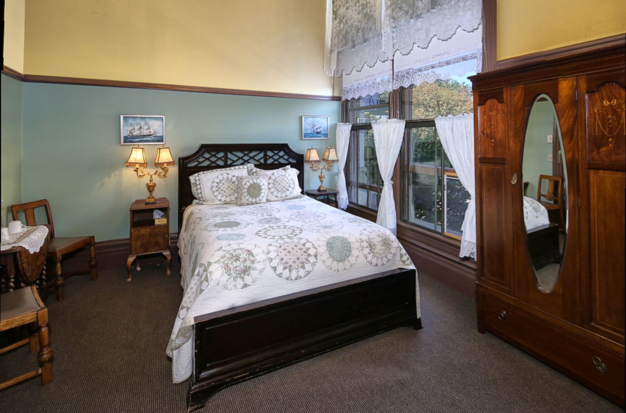 Une chambre à coucher avec un grand lit, une armoire en bois, deux tables de chevet avec des lampes, une chaise et une fenêtre avec des rideaux.