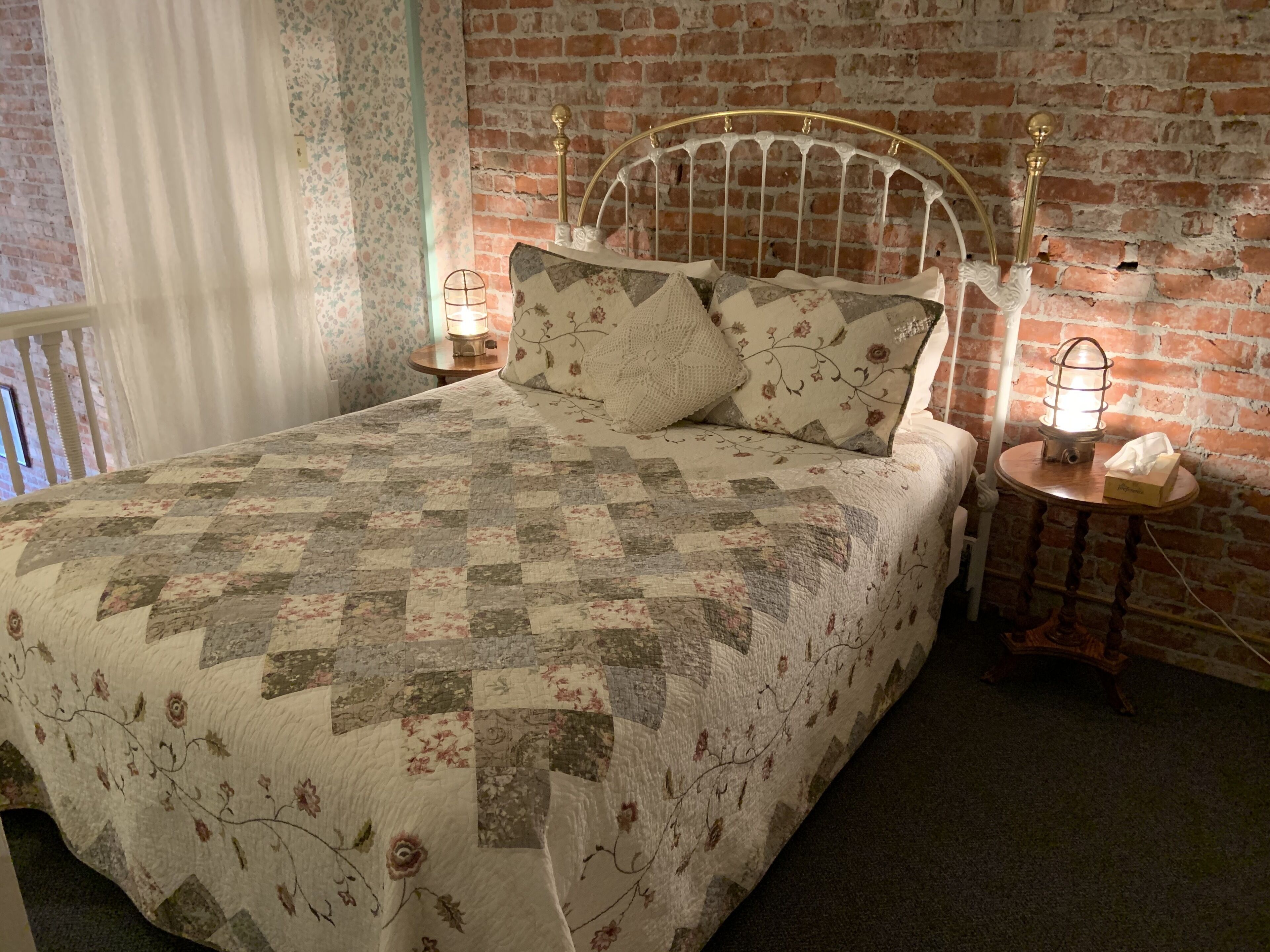 A bed with a quilt, a headboard, two bedside tables with lamps, and a brick wall.