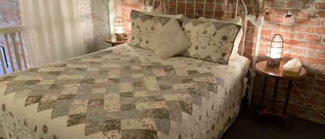 A bed with a quilt, a headboard, two bedside tables with lamps, and a brick wall.