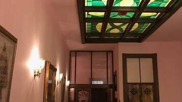 A hallway with a stained glass ceiling, wall-mounted lights, and framed artwork.