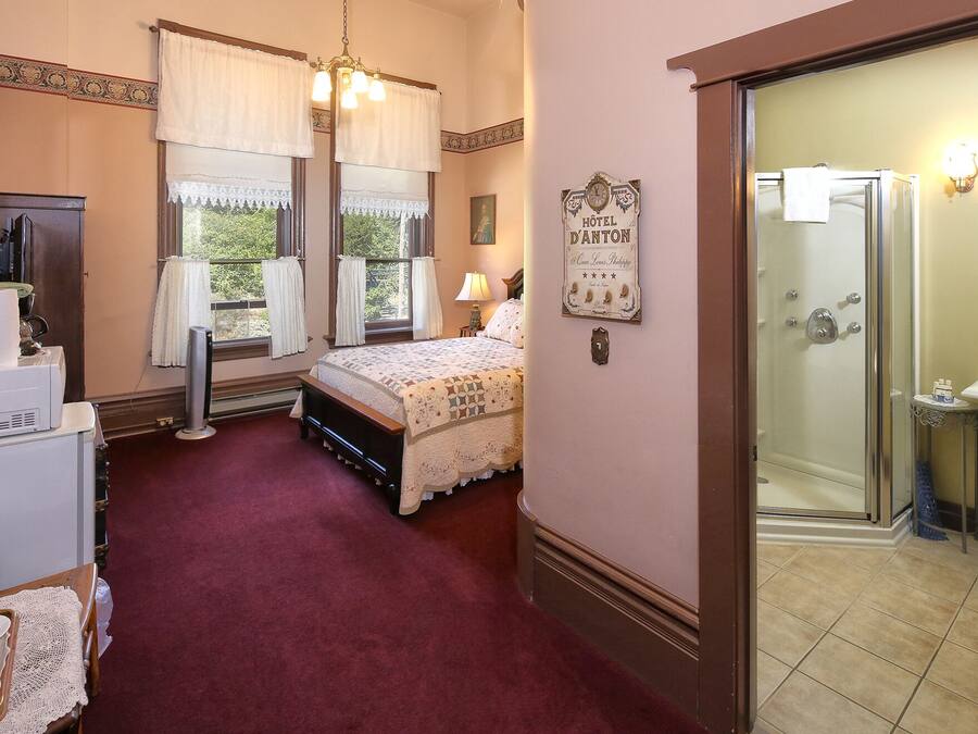 A hotel room with a bed, a desk with a lamp, a shower, and a sign on the wall.