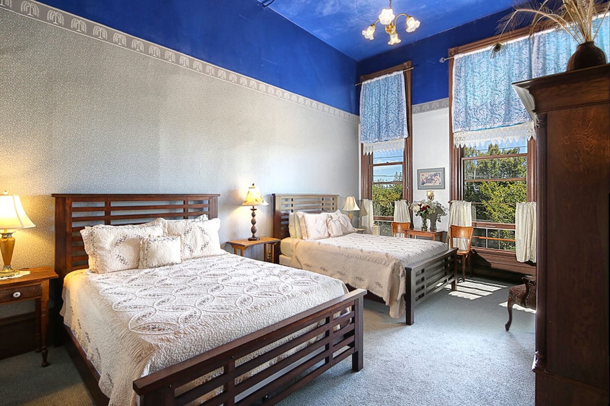 A bedroom with two beds, wooden headboards, and a large window with curtains.