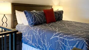 Un lit bien fait, recouvert d’une couvre-lit aux motifs de branches d’arbres bleues et blanches, avec une tête de lit en bois et deux lampes de chevet.