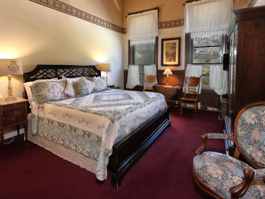 A traditional bedroom with a large bed, two bedside tables, a wooden chair, and a wooden wardrobe.