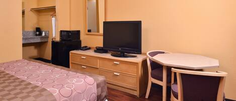 Una habitación de hotel con una cama, un escritorio con televisor, una silla, un aparador y un espejo.