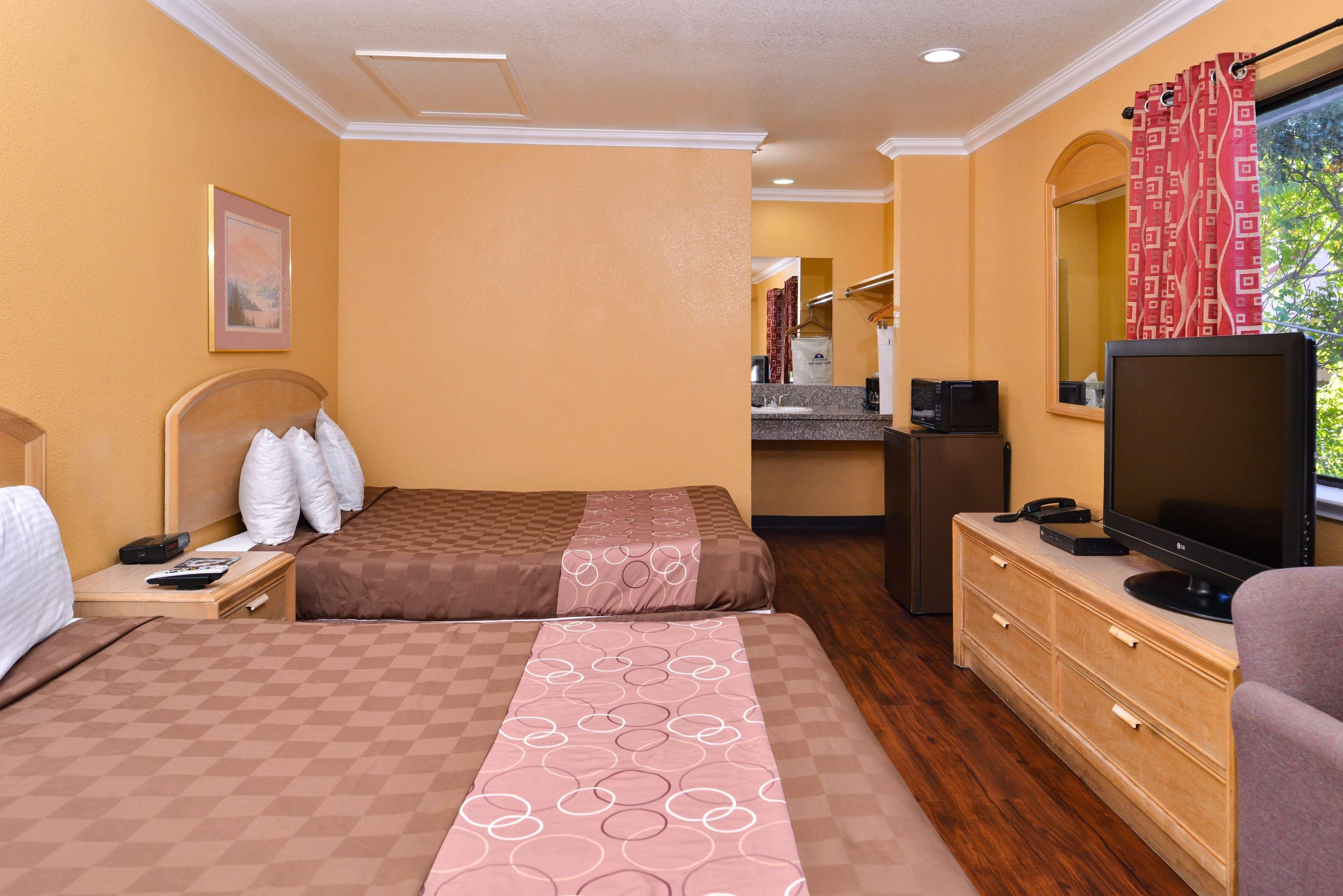 Una habitación de hotel con dos camas, una televisión, un escritorio con una computadora y un baño visible al fondo.