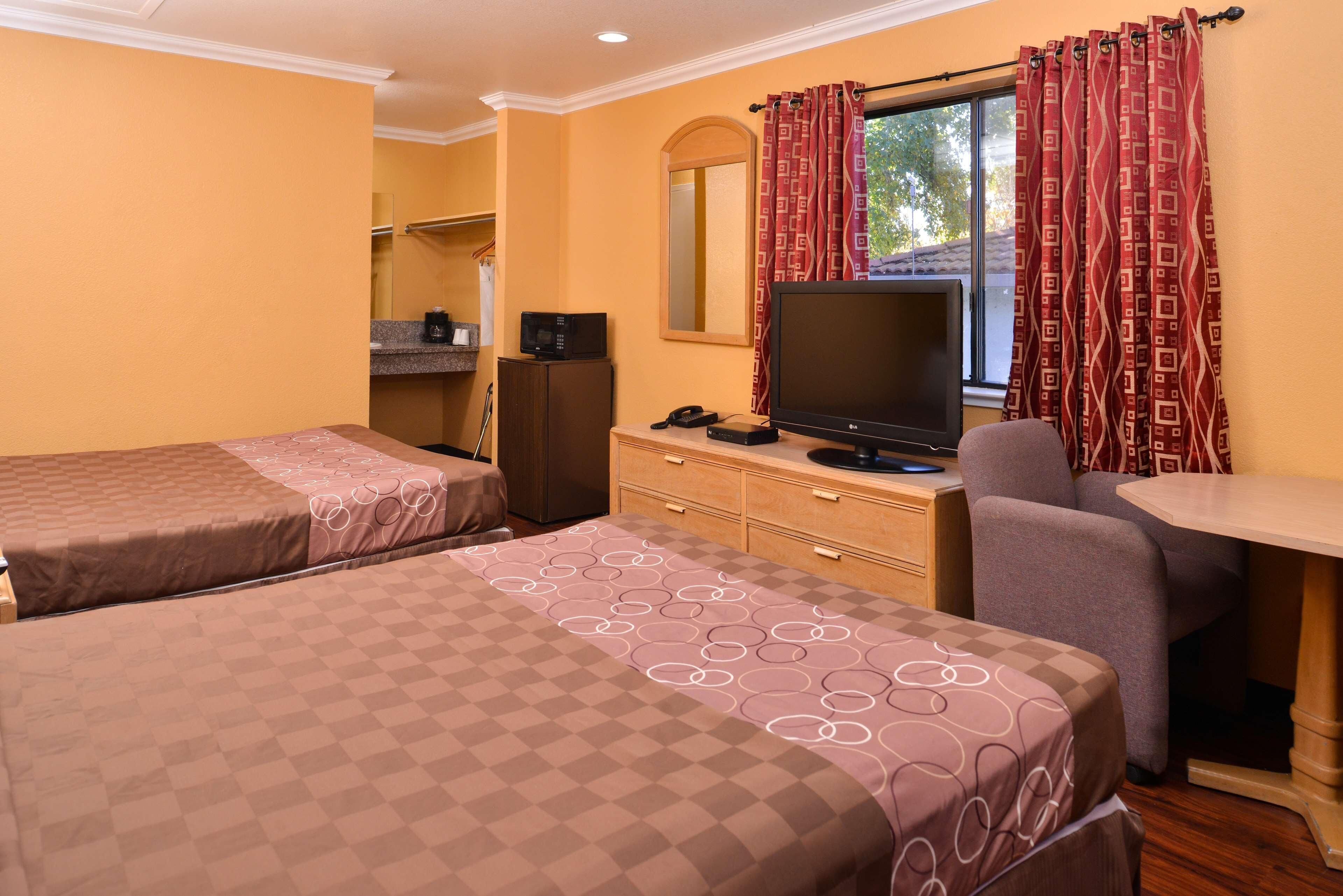 Habitación de hotel con dos camas, un escritorio, un televisor, un espejo y una ventana con cortinas.