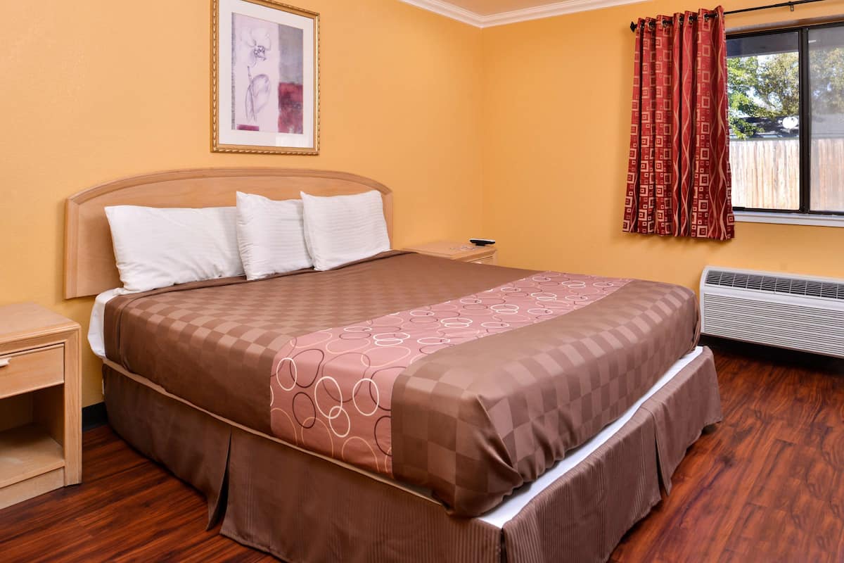 Een net opgemaakt bed met een bruin-wit geruit sprei, een houten hoofdbord en een nachtkastje met een lamp.