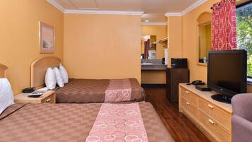 Quarto de hotel com duas camas, televisão, escrivaninha e banheiro ao fundo.