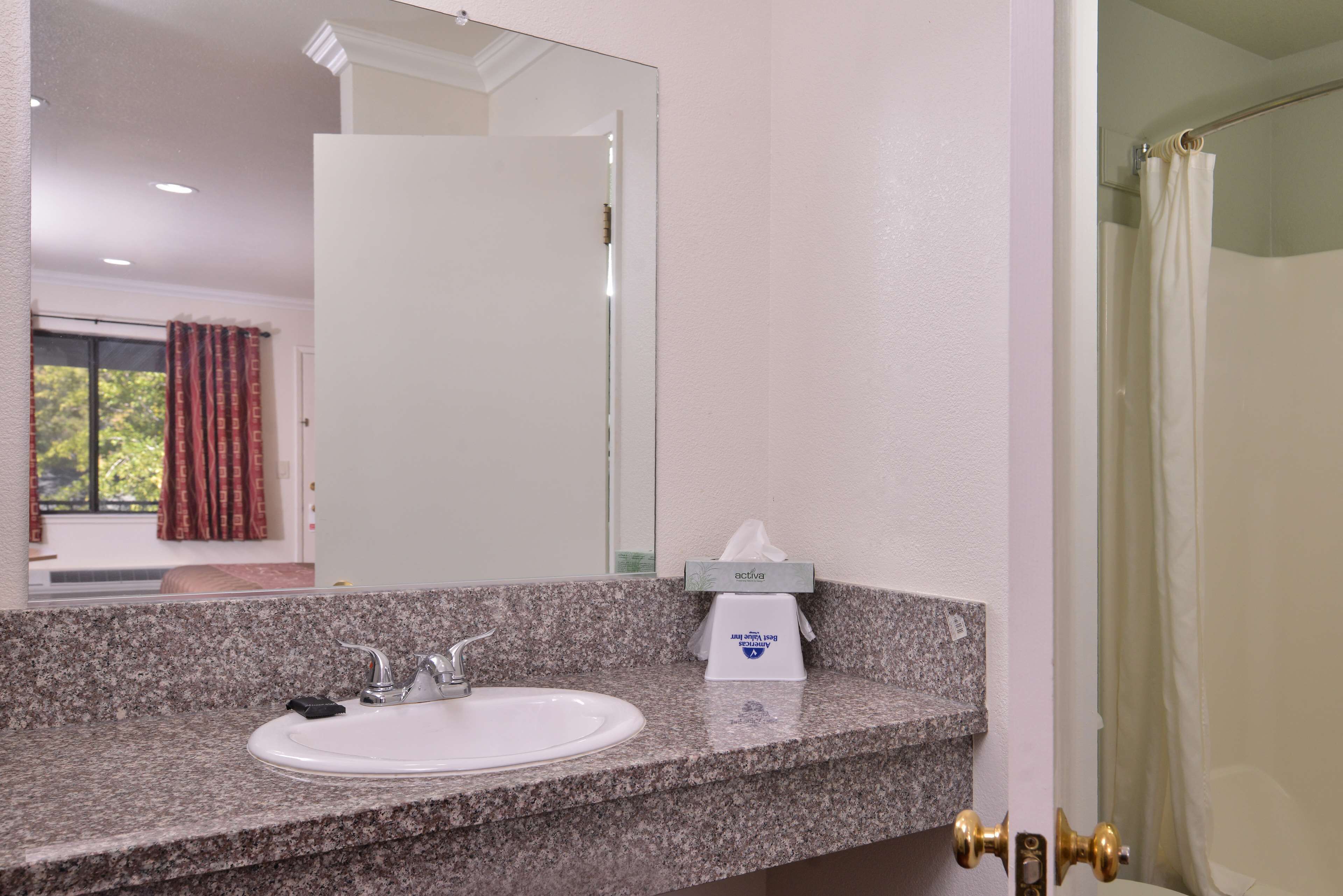 A bathroom with a granite countertop, a white sink, a mirror, and a tissue box.