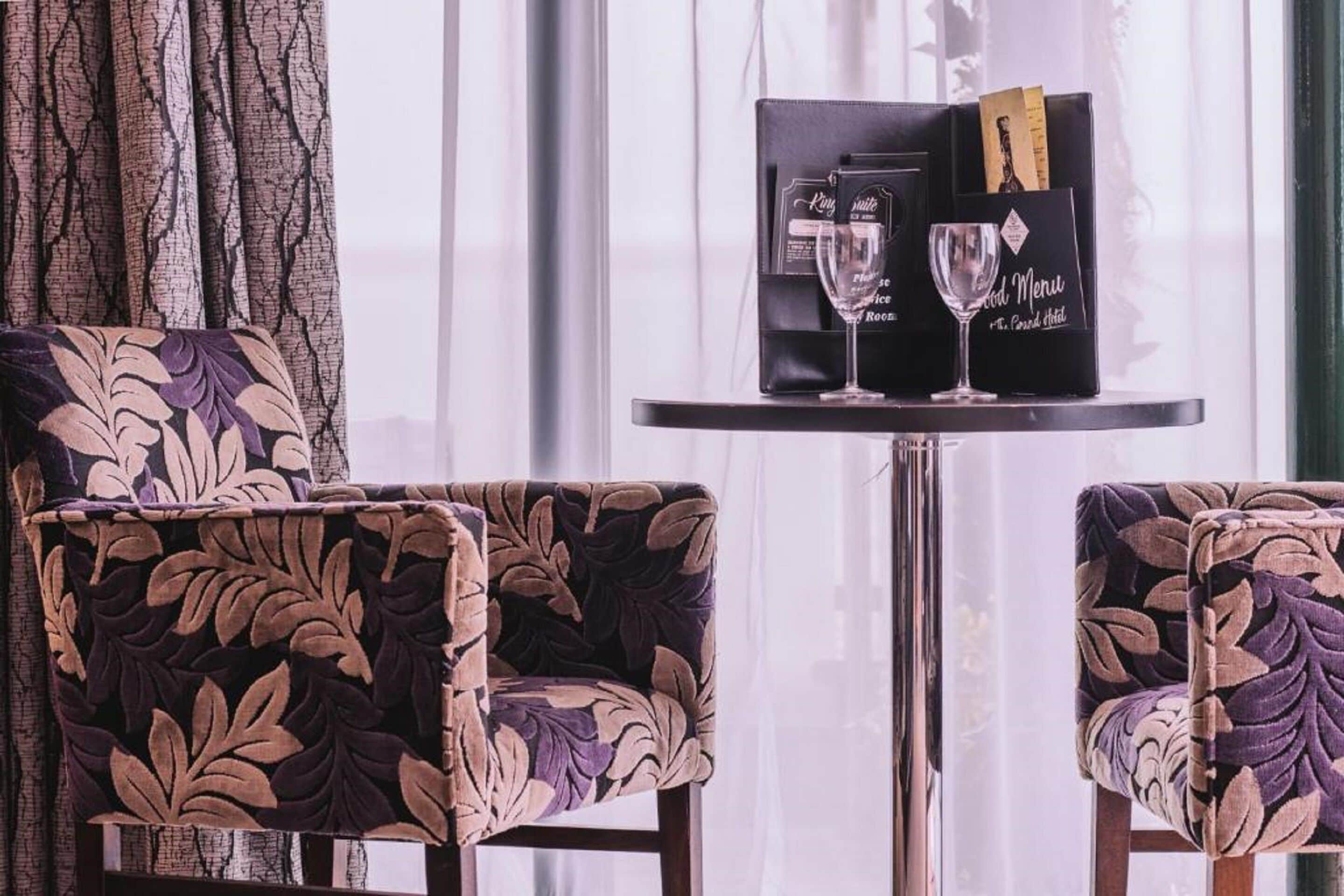 A room with two patterned armchairs, a table with a menu, and a book.