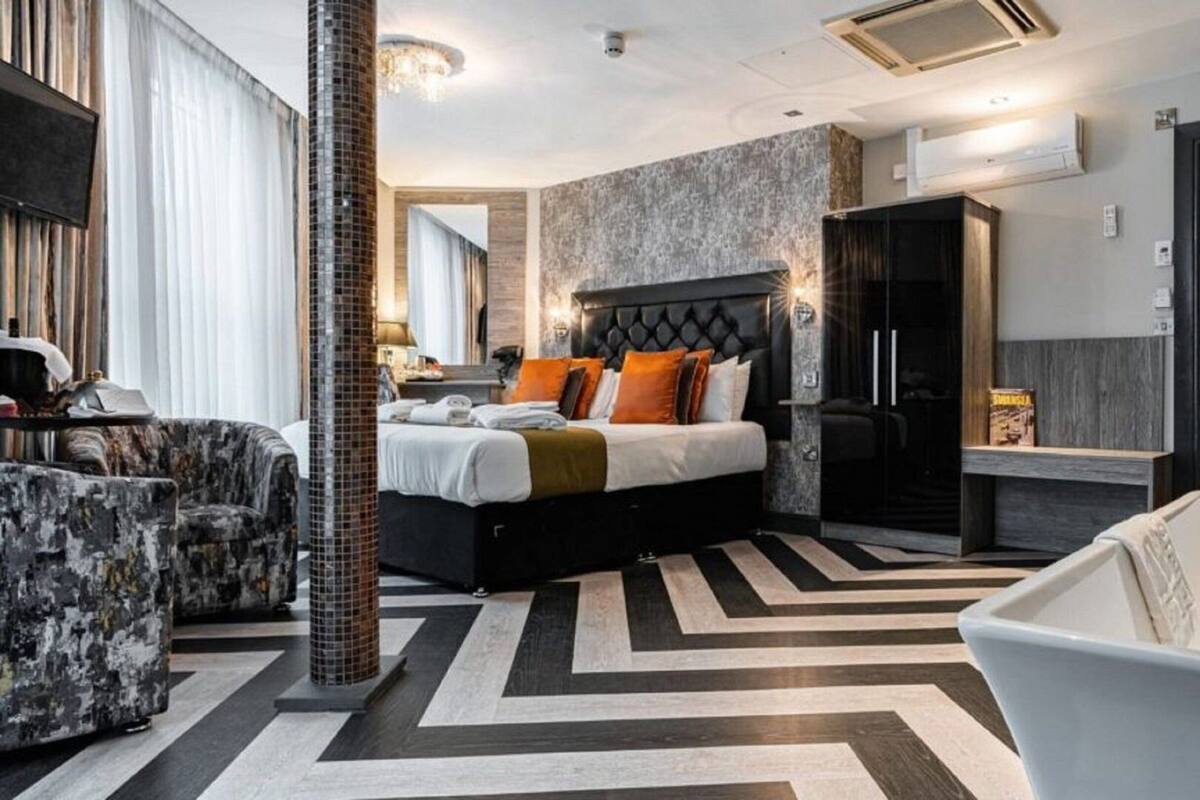 Une chambre d’hôtel moderne avec un grand lit, un coin salon avec un fauteuil, une baignoire et une armoire.