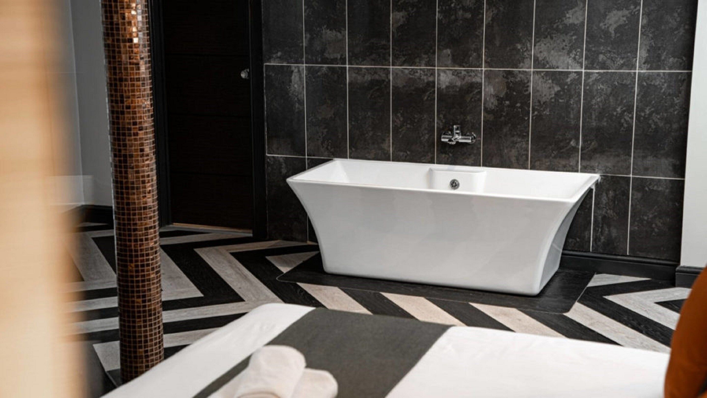 Ein modernes Badezimmer mit einer freistehenden Badewanne, schwarzen Fliesenwänden und einem geometrisch gemusterten Boden.
