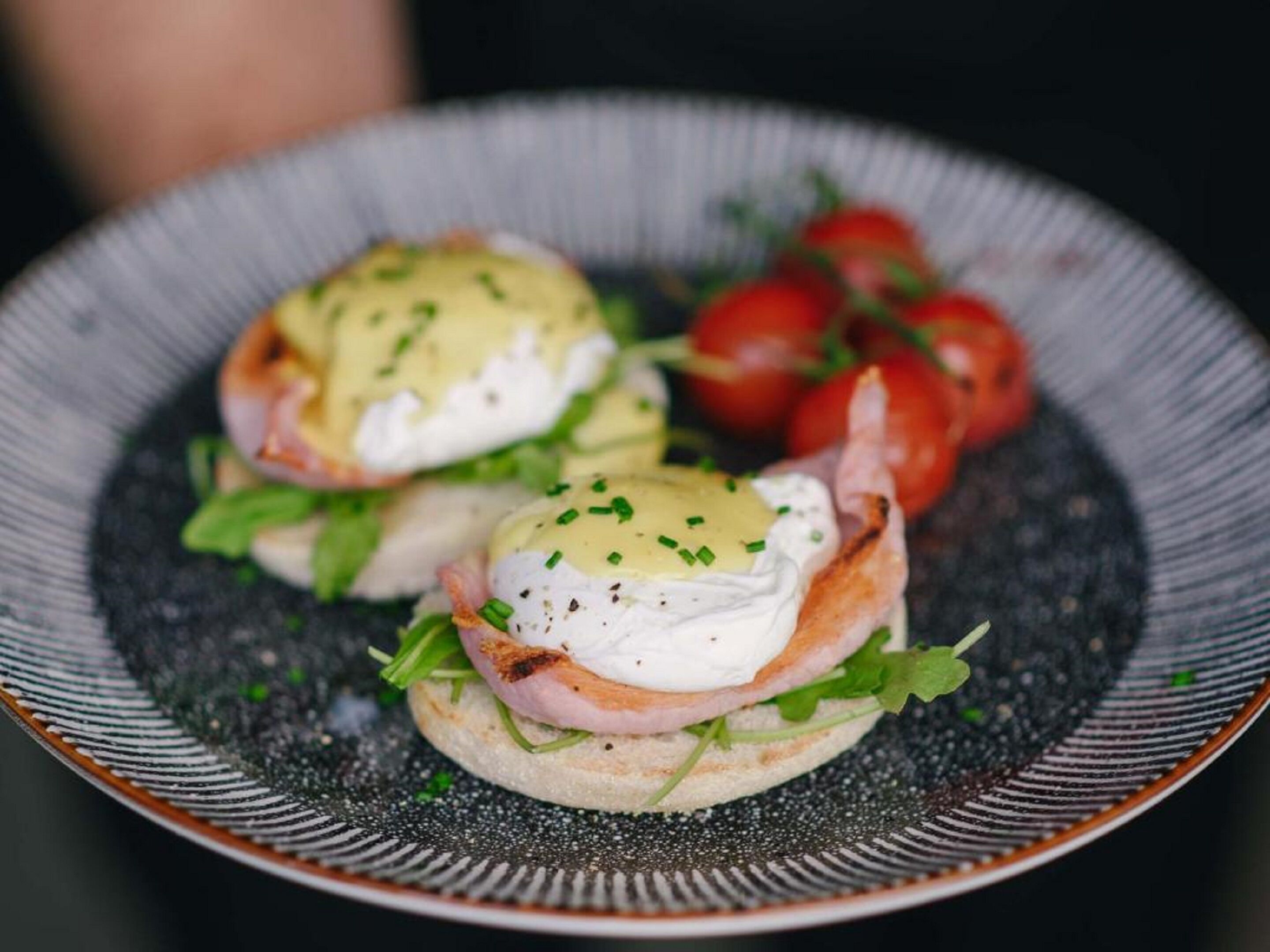 A plate with two poached eggs on toast, garnished with chives, and accompanied by cherry tomatoes.