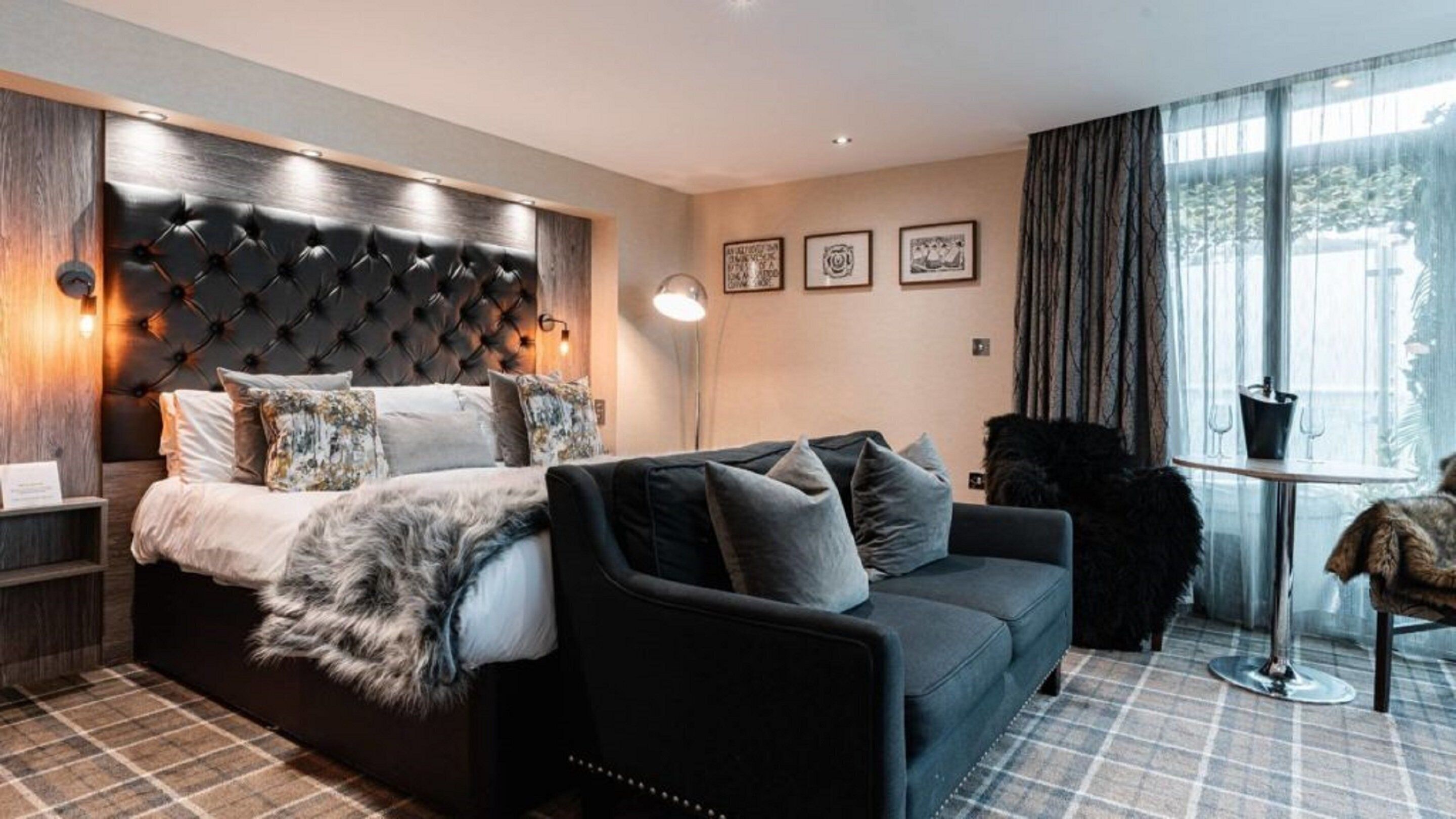 A hotel room with a large bed, a sofa, a small table, and a window with curtains.