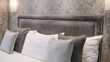 Uma cama com cabeceira estofada cinza, roupa de cama branca e almofadas cinzas.