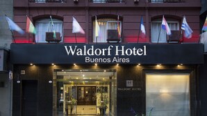 The exterior of Waldorf Hotel in Buenos Aires, featuring a prominent entrance with glass doors, a black facade, and multiple flags displayed above. - Waldorf Hotel (Buenos Aires)