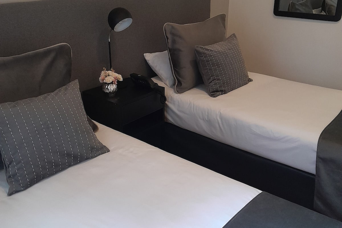 Una habitación de hotel con dos camas, una mesita de noche con lámpara y un espejo en la pared.