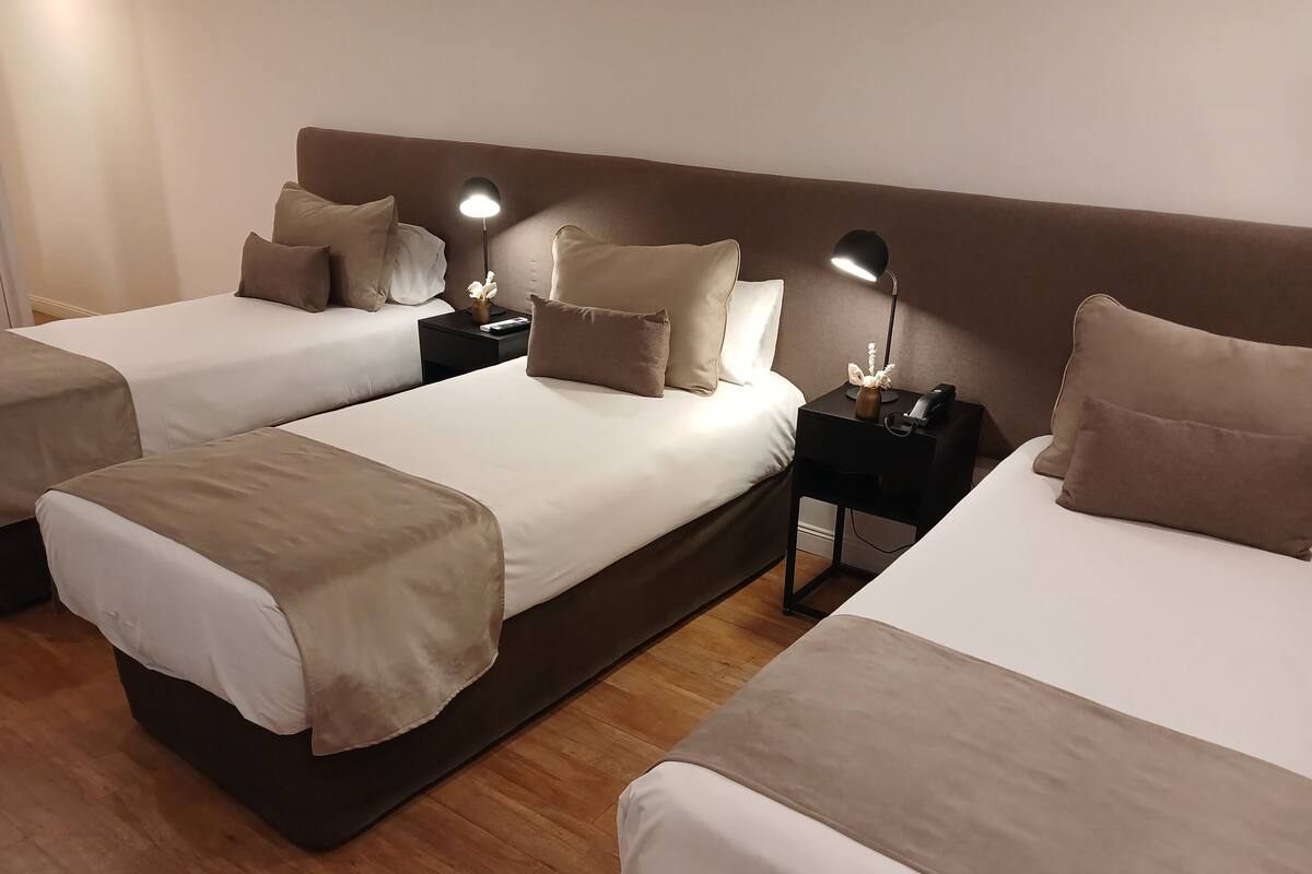 Habitación de hotel con dos camas, cada una con una mesita de noche, una lámpara y un jarrón con flores.