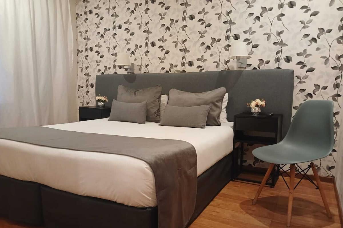 A bedroom with a large bed, a nightstand with a lamp, a chair, and a wall with a leaf pattern.