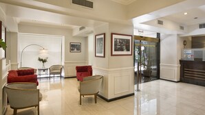A spacious lobby with a red sofa, two armchairs, a small table with a vase, and framed pictures on the wall. - Waldorf Hotel (Buenos Aires)