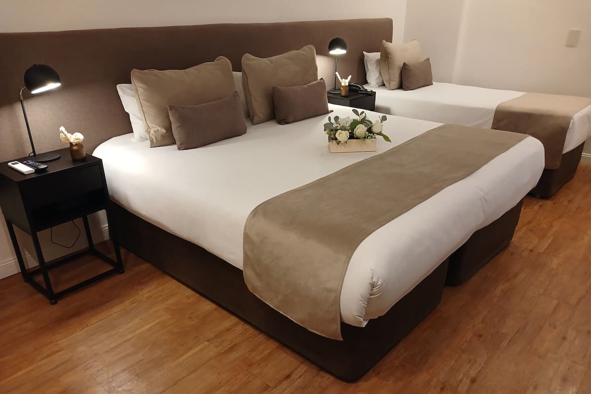 A hotel room with two beds, a nightstand with a lamp, and a small table with a vase of flowers.