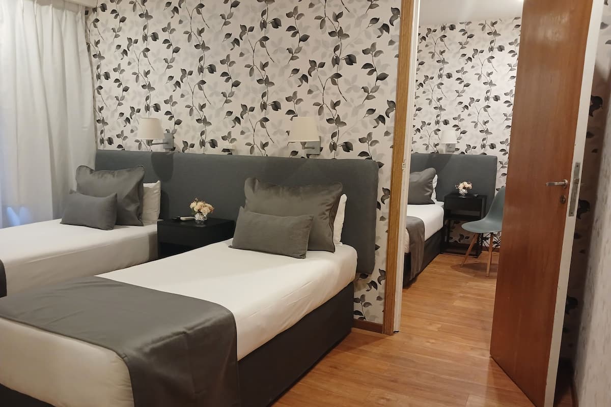 A hotel room with two beds, a wooden floor, and a floral wallpaper.