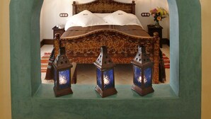 A bedroom with a bed centered under a large archway, two wall-mounted lamps, and two lanterns on the floor. - Alcoba del Rey de Sevilla Boutique Hotel (Seville)