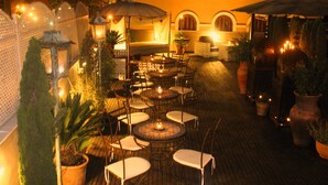 An outdoor patio with round tables and chairs, potted plants, and string lights. - Alcoba del Rey de Sevilla Boutique Hotel (Seville)
