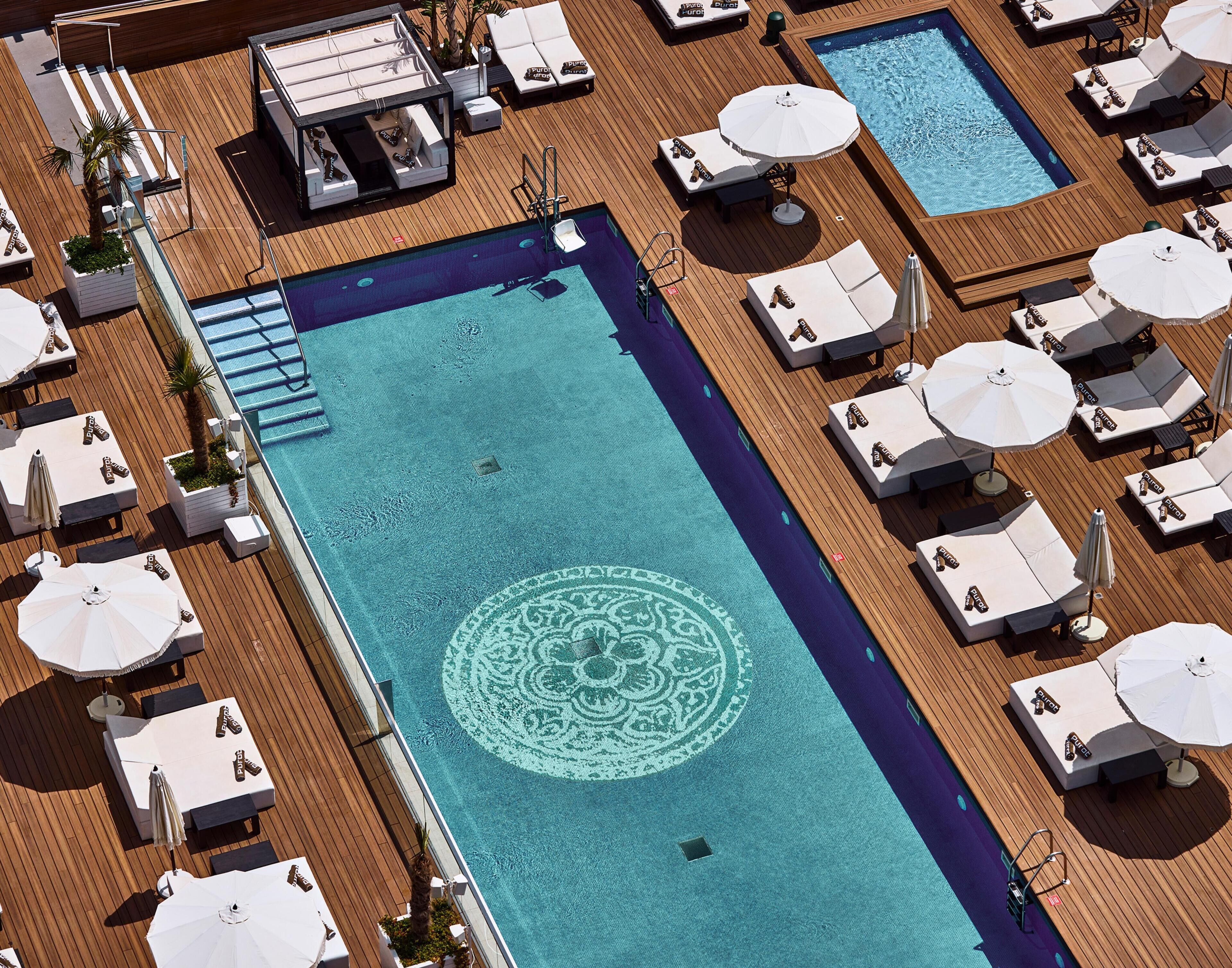 Une grande piscine au design géométrique, entourée de chaises longues et de parasols.