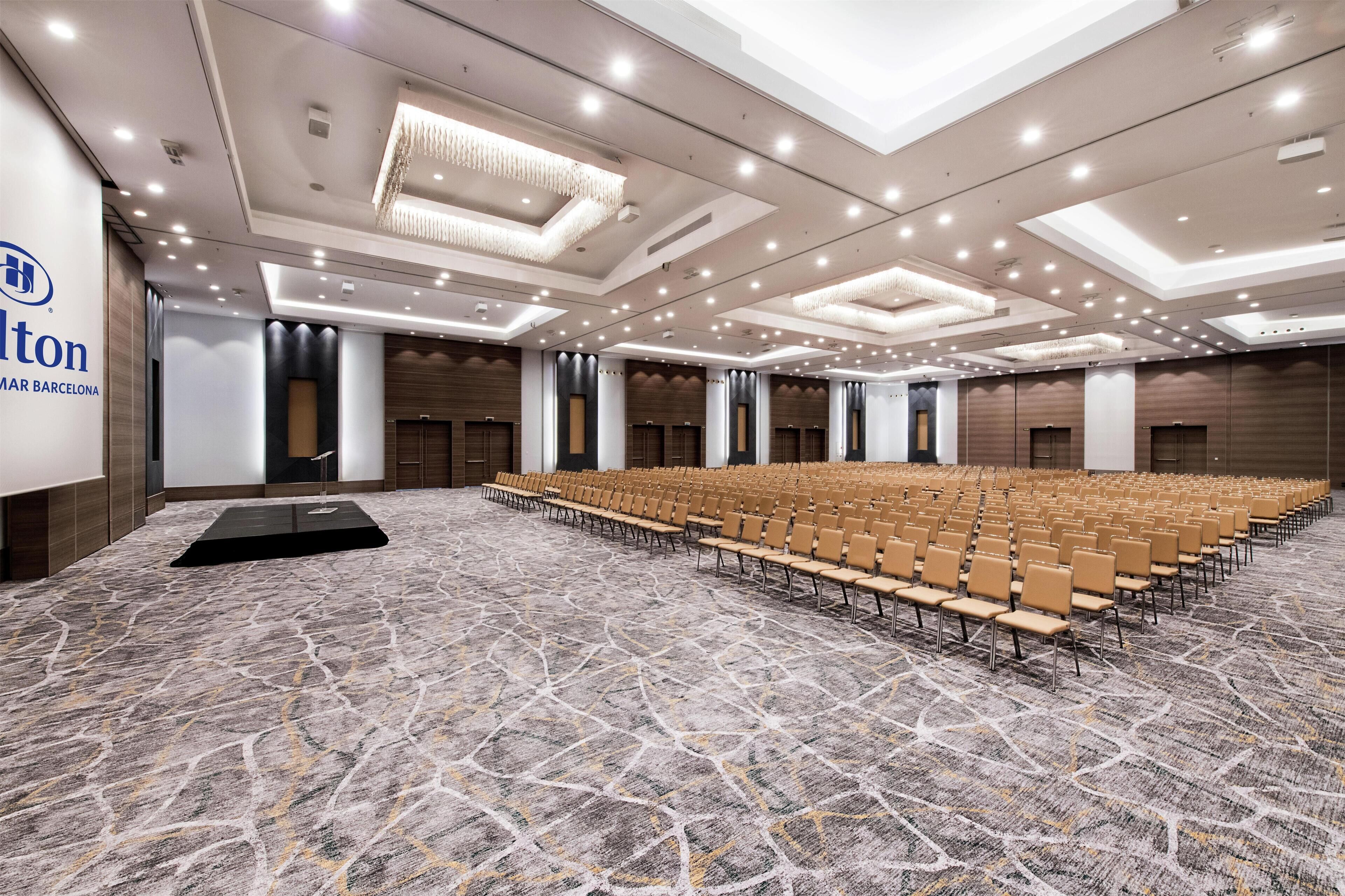 Un amplio salón de conferencias con filas de sillas, un atril y suelo alfombrado.