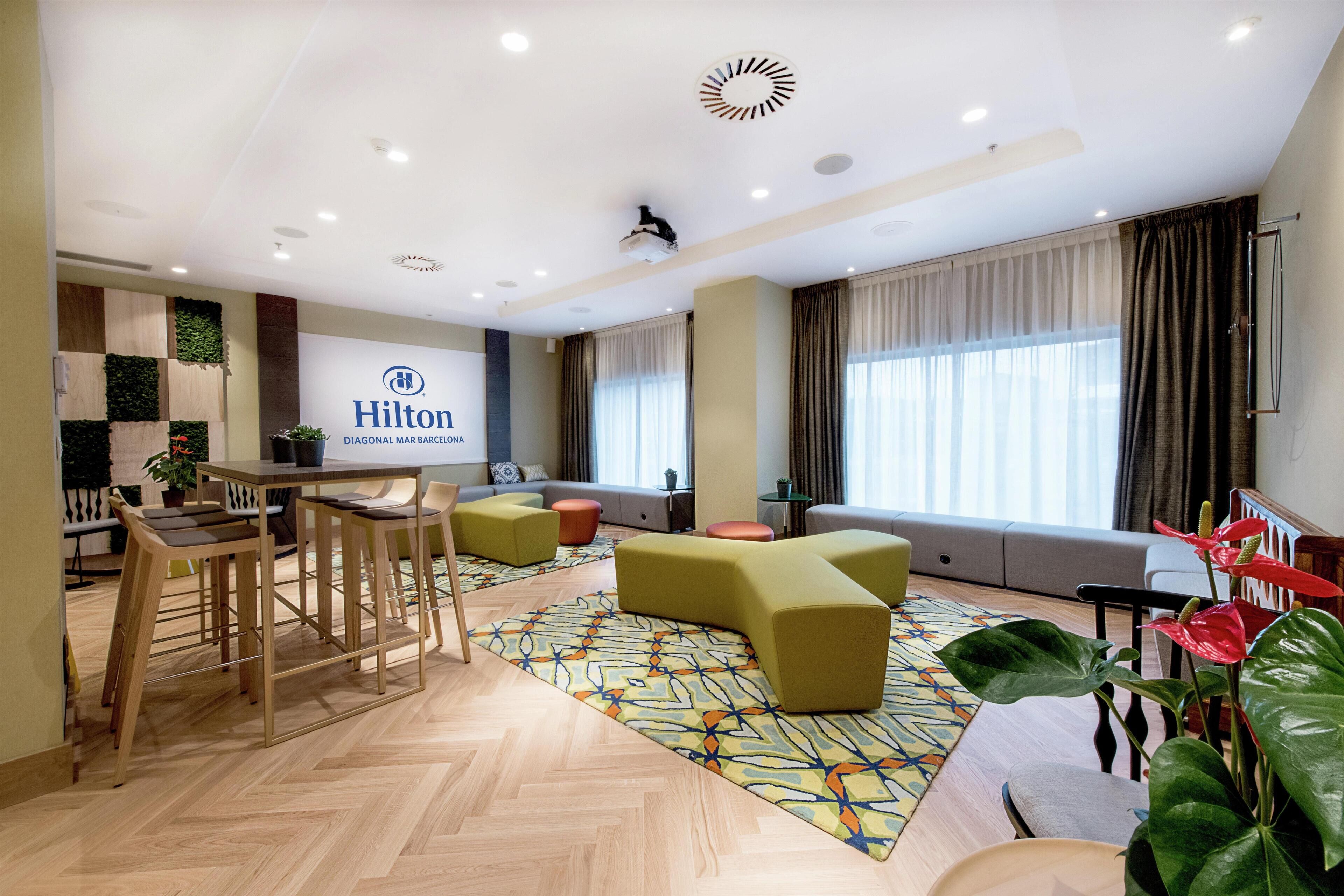 Um hall de hotel moderno com balcão de recepção, área de estar e uma grande janela com cortinas.