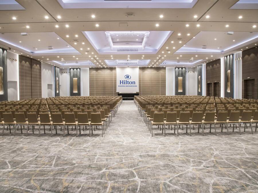 A spacious conference room with rows of chairs, a large Hilton banner, and a modern ceiling design.