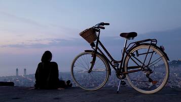 A bicycle with a basket and a seat, positioned on a flat surface with a cityscape in the background.