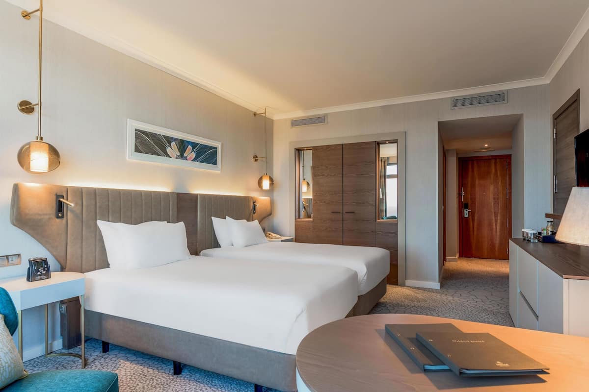 A hotel room with two beds, a desk, a chair, a TV, and a wardrobe.