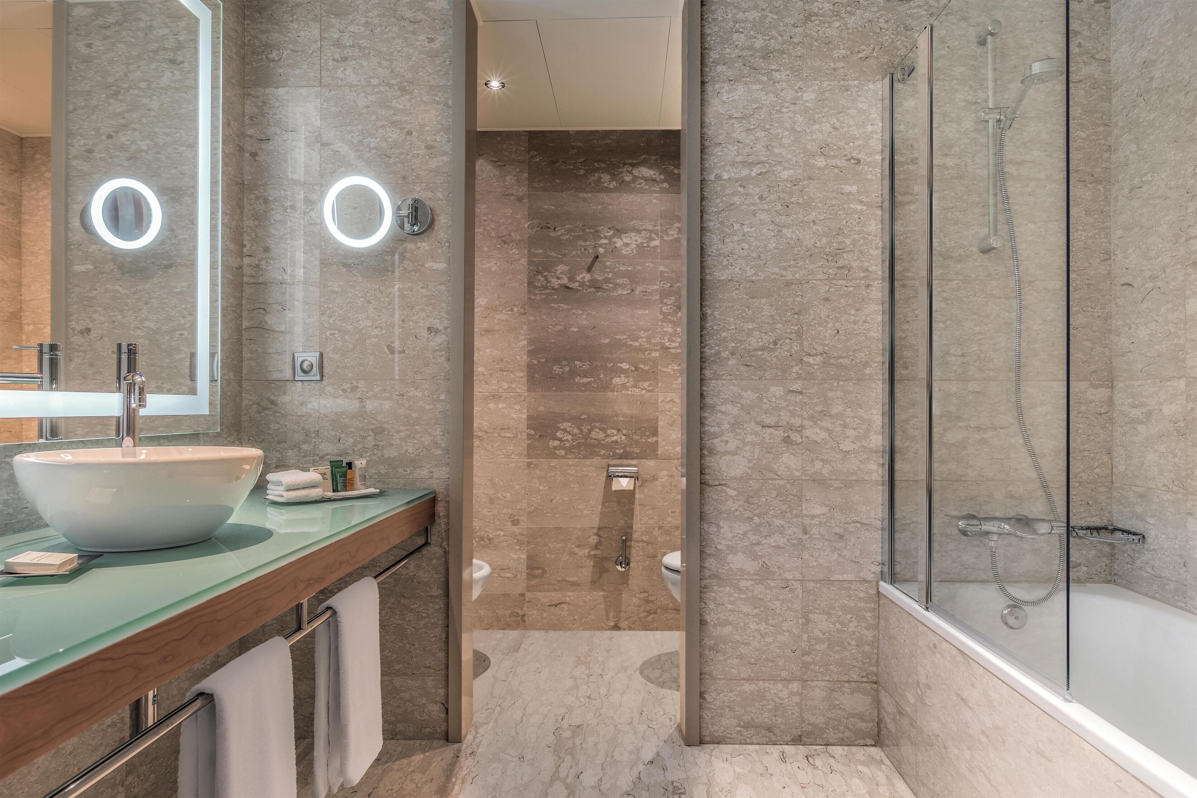A modern bathroom with a large sink, a glass-enclosed shower, and a marble-tiled floor.