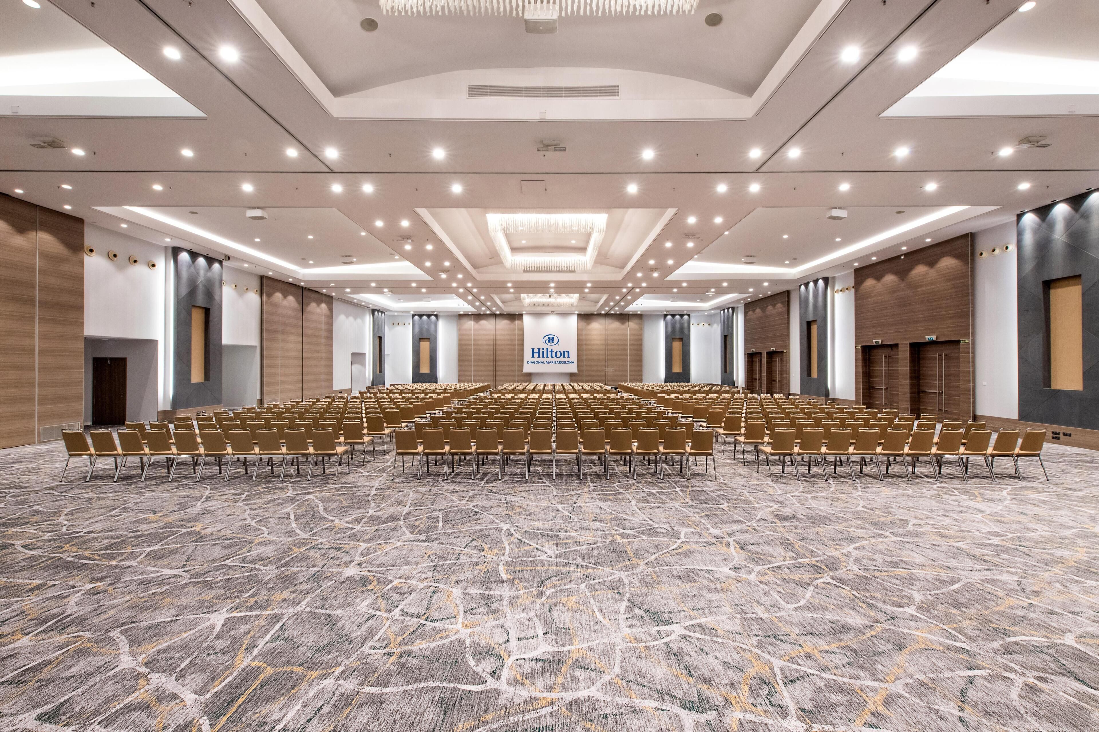 Un amplio salón de conferencias bien iluminado, con filas de sillas y un escenario al frente.